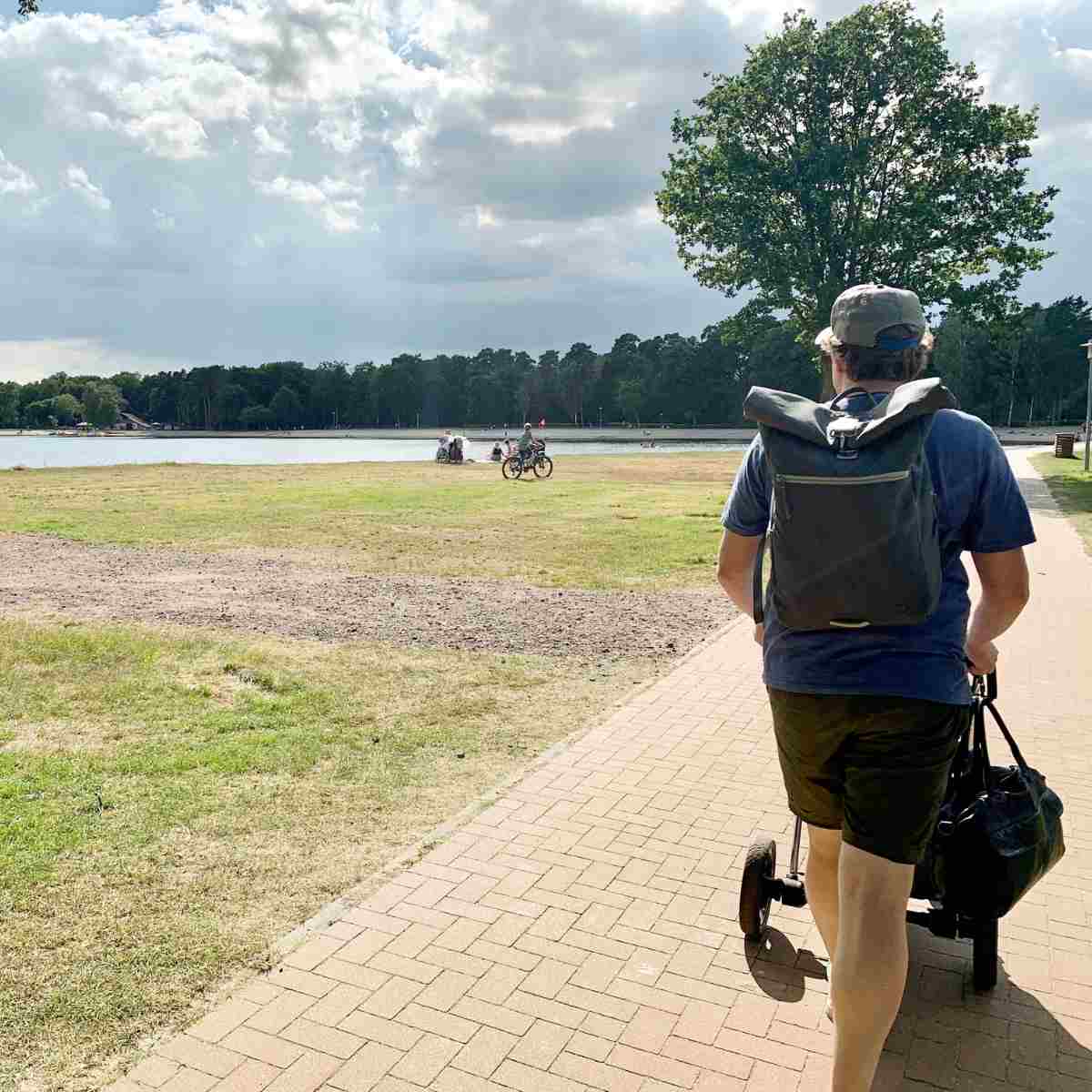 Mann geht mit einem Kinderwagen spazieren und traegt den FUCHS UND REBELL PIET Rolltop Rucksack in dunkelgrau als Wickelrucksack.