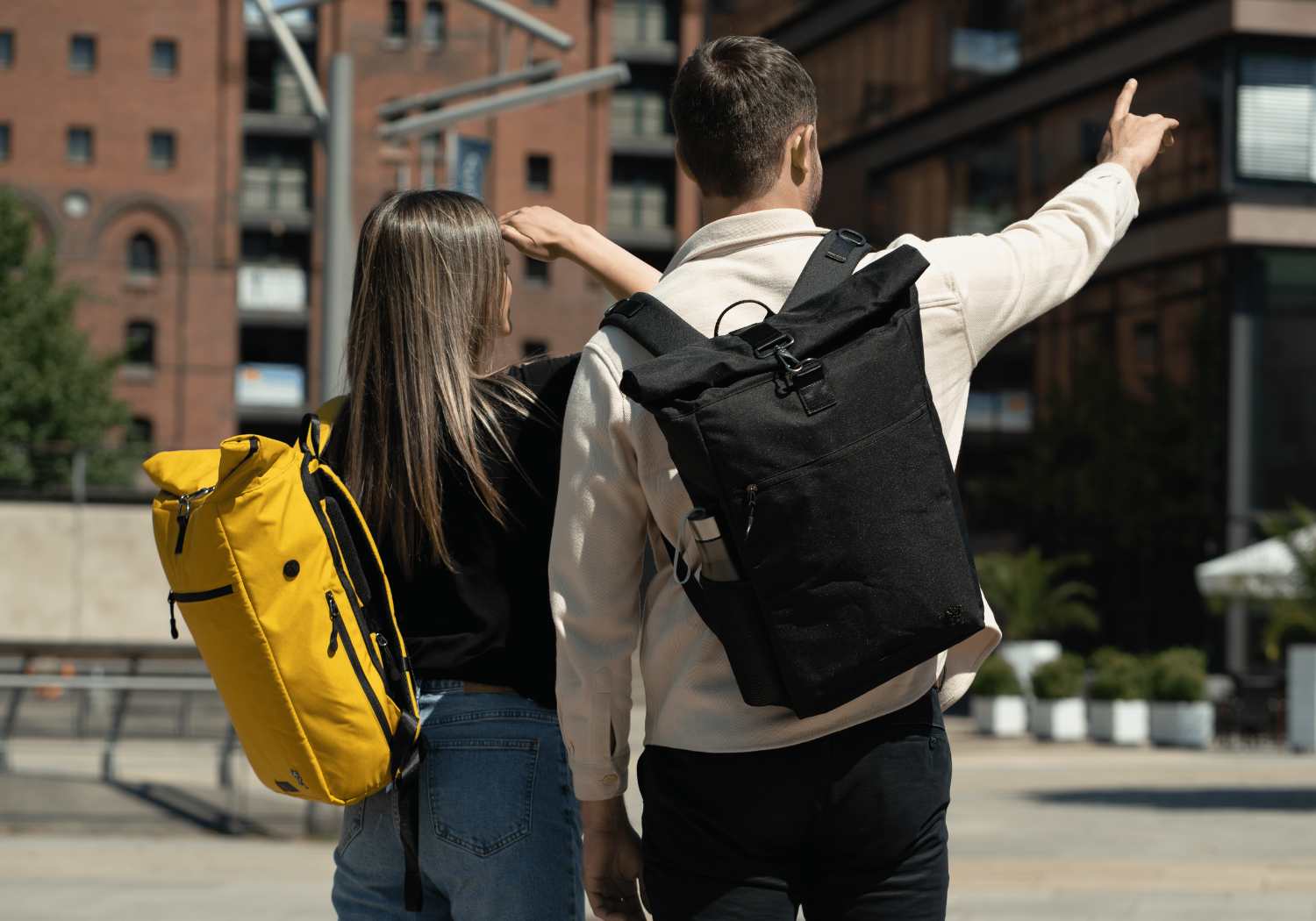 Junges Paar geht in der Hamburger Speicherstadt spazieren und traegt den FUCHS und REBELL Rolltop Rucksack PIET in schwarz und senfgelb .