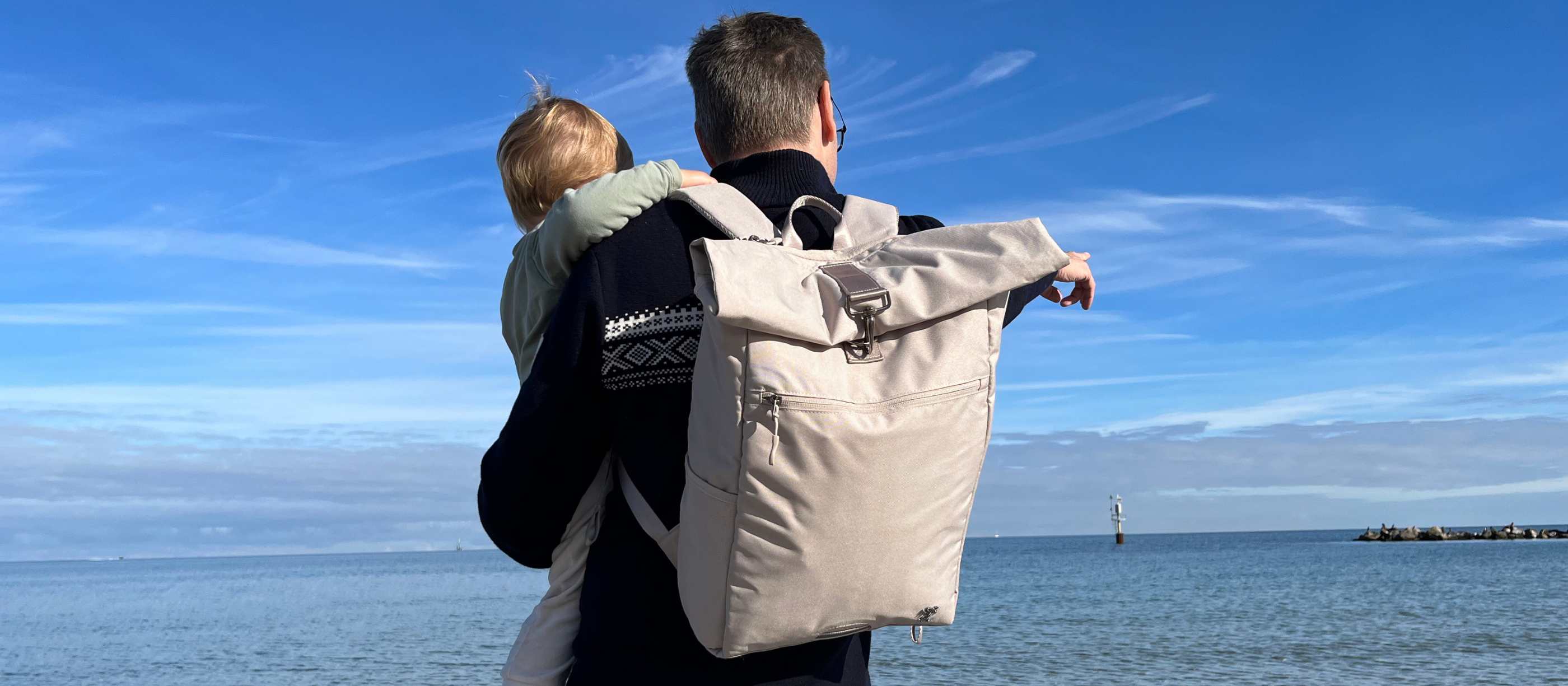 Mann mit dem FUCHS und REBELL PIET Rolltop Rucksack in beige und Kind am Strand