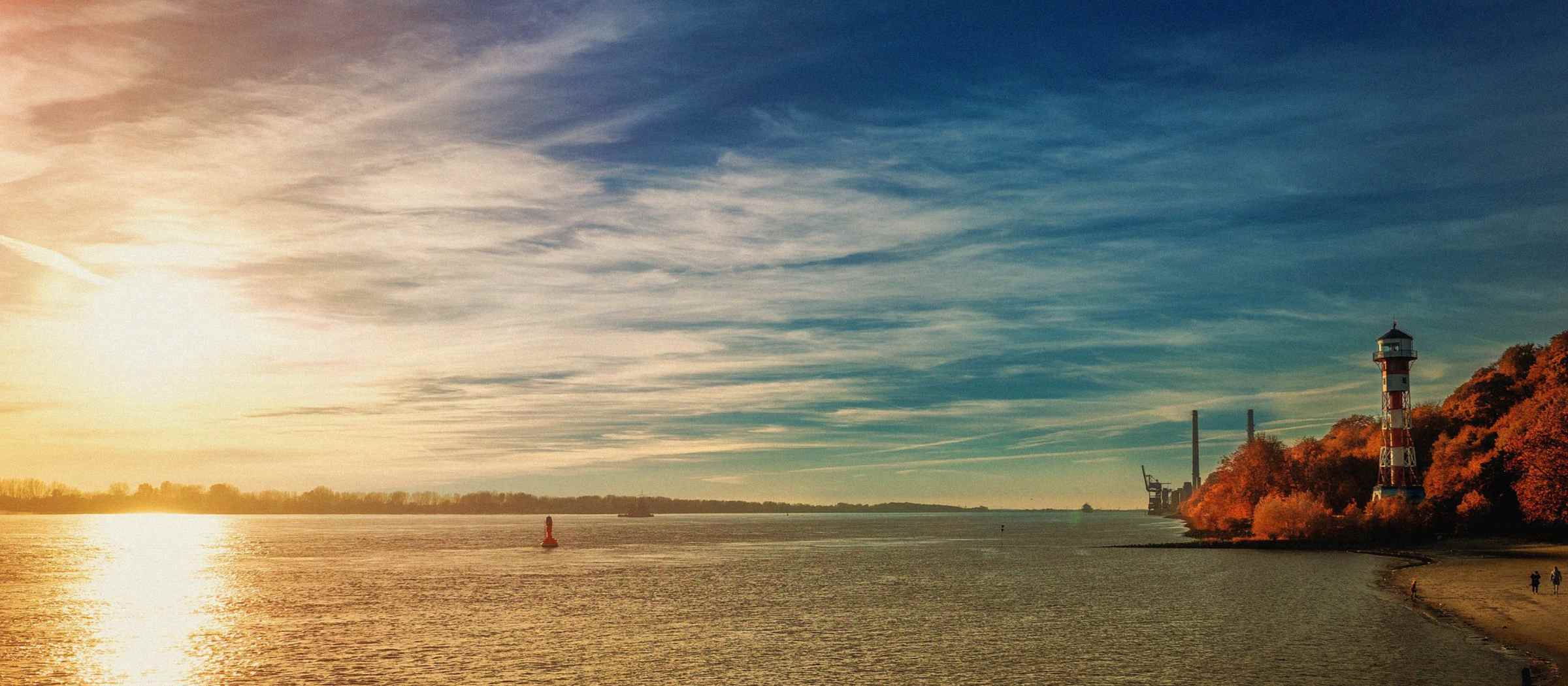 Das Foto zeigt die Elbe und einen Leuchtturm bei Sonnenuntergang