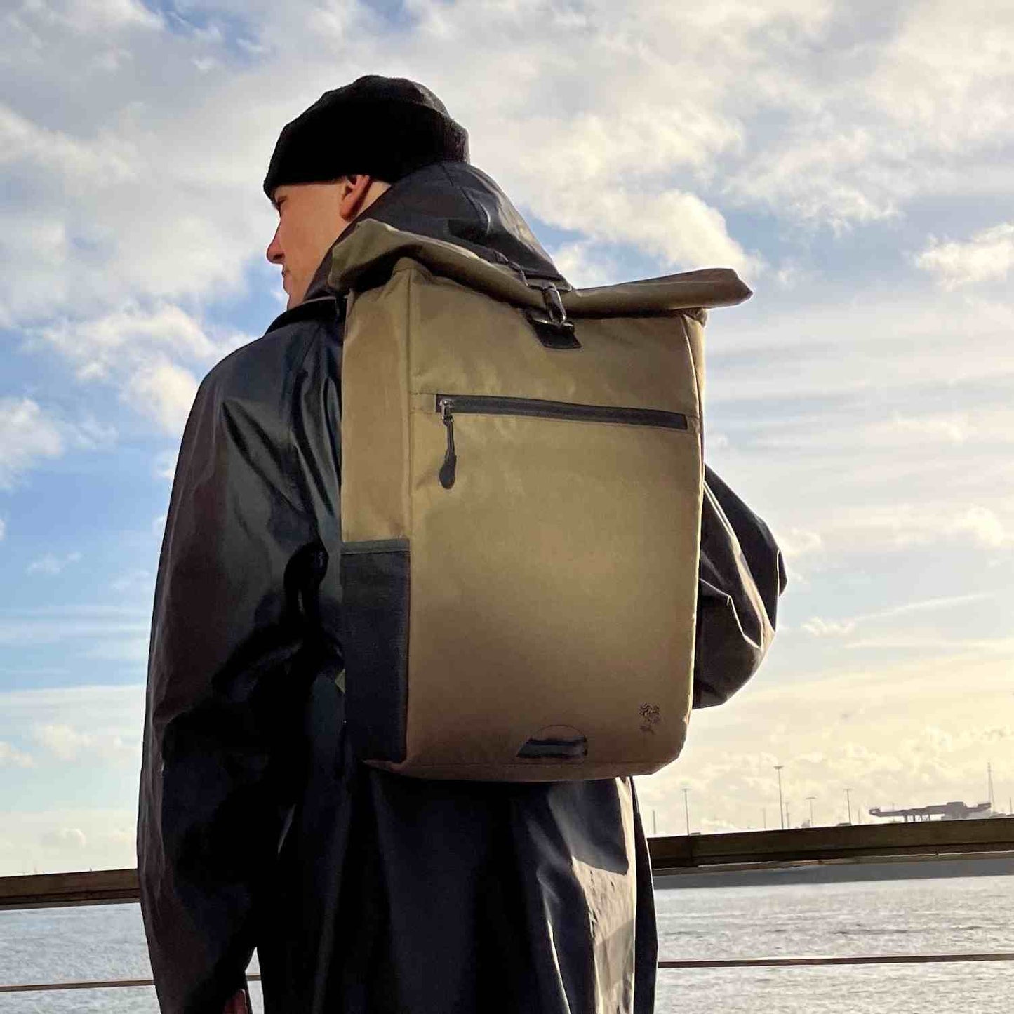 Gutaussehender Mann geht an der Elbe spazieren mit dem oliv gruenen PIET Rolltop Rucksack.