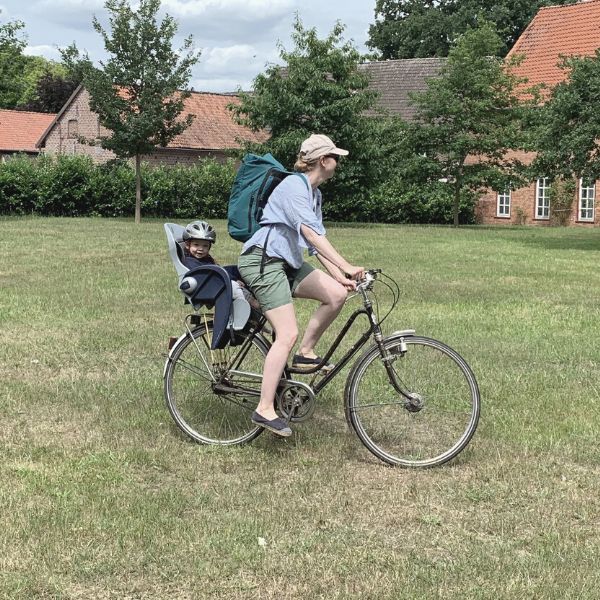 Junge Mutter fährt mit ihrem Kind Fahrrad und traegt den dunkelgrauen FUCHS & REBELL PIET Rolltop Rucksack