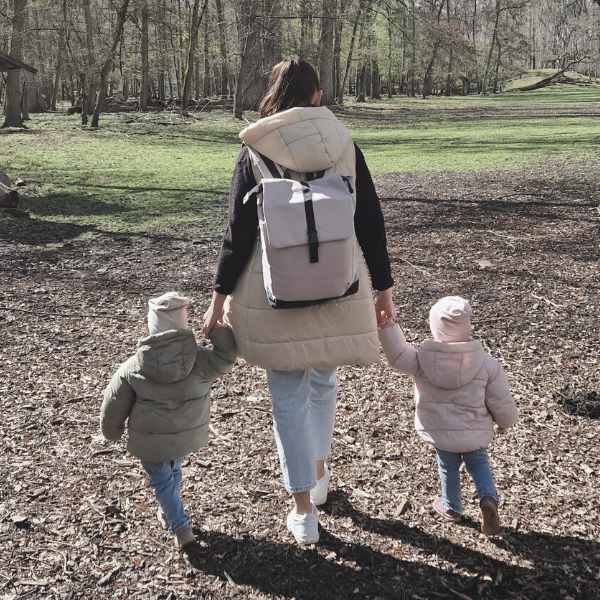 Junge Mutter geht im Wald mit ihren Zwillingen im Kleinkindalter im Wald spazieren. Sie traegt den beigefarbenen MATS Daypack von FUCHS & REBELL.