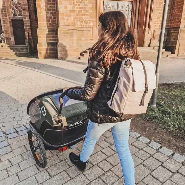 Junge Mutter schiebt ihren Kinderwagen durch die Stadt und traegt den beigefarbenen FUCHS & REBELL MATS Daypack