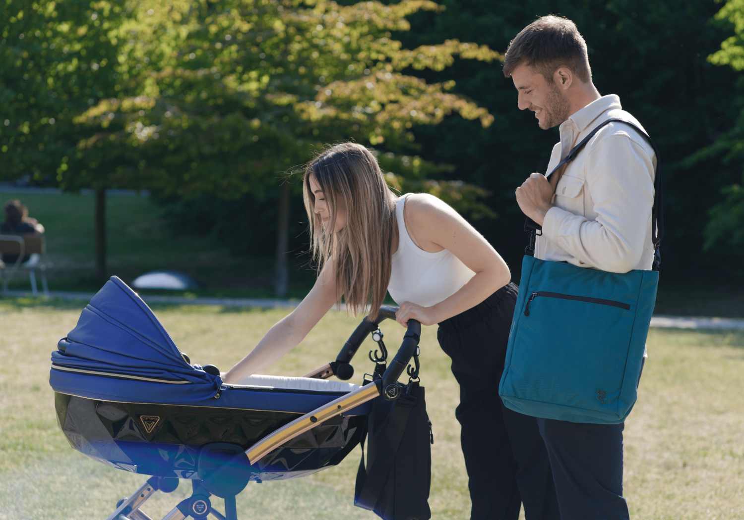 Junges Paar geht mit ihrem Kind im Kinderwagen spazieren. Beide tragen die FUCHS UND REBELL Umhangetasche JONA in schwarz und pretrol blau. 