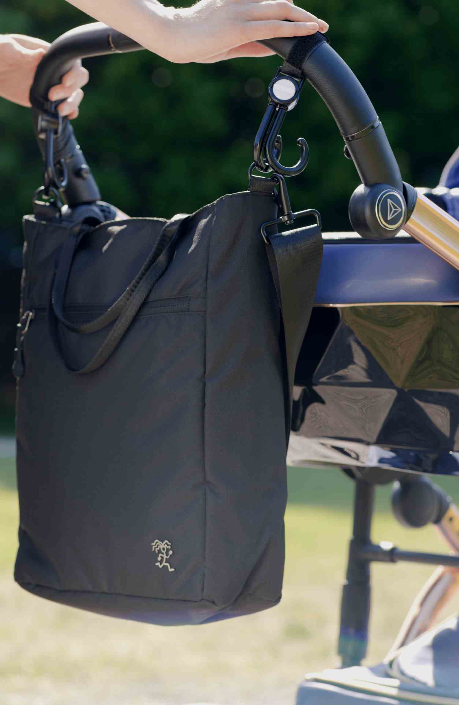 DIE FUCHS und REBELL Umhaengetasche JONA in schwarz hängt als Wickeltasche an einem Kinderwagen