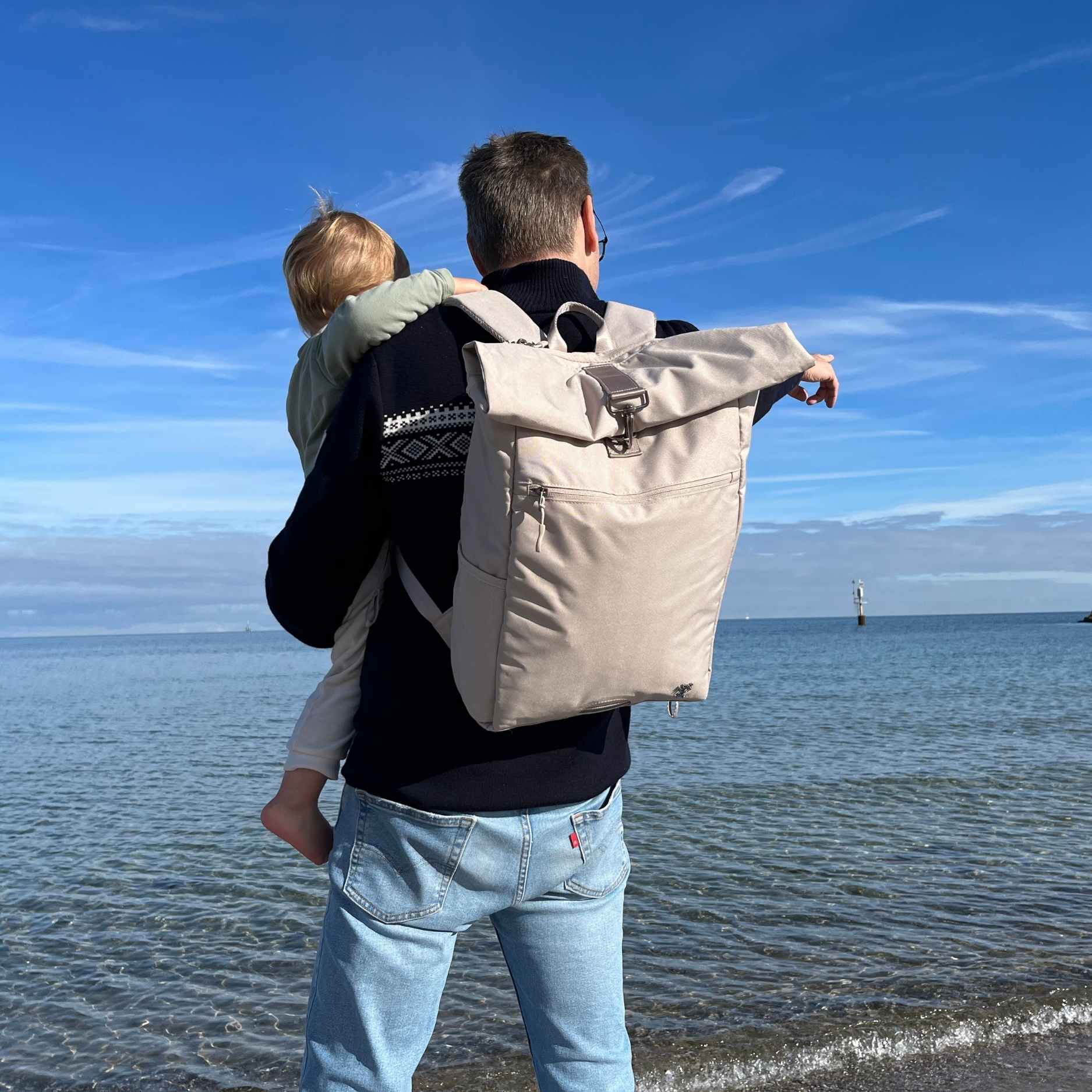 Mann traegt den FUCHS und REBELL PIET Rolltop Rucksack in beige. 