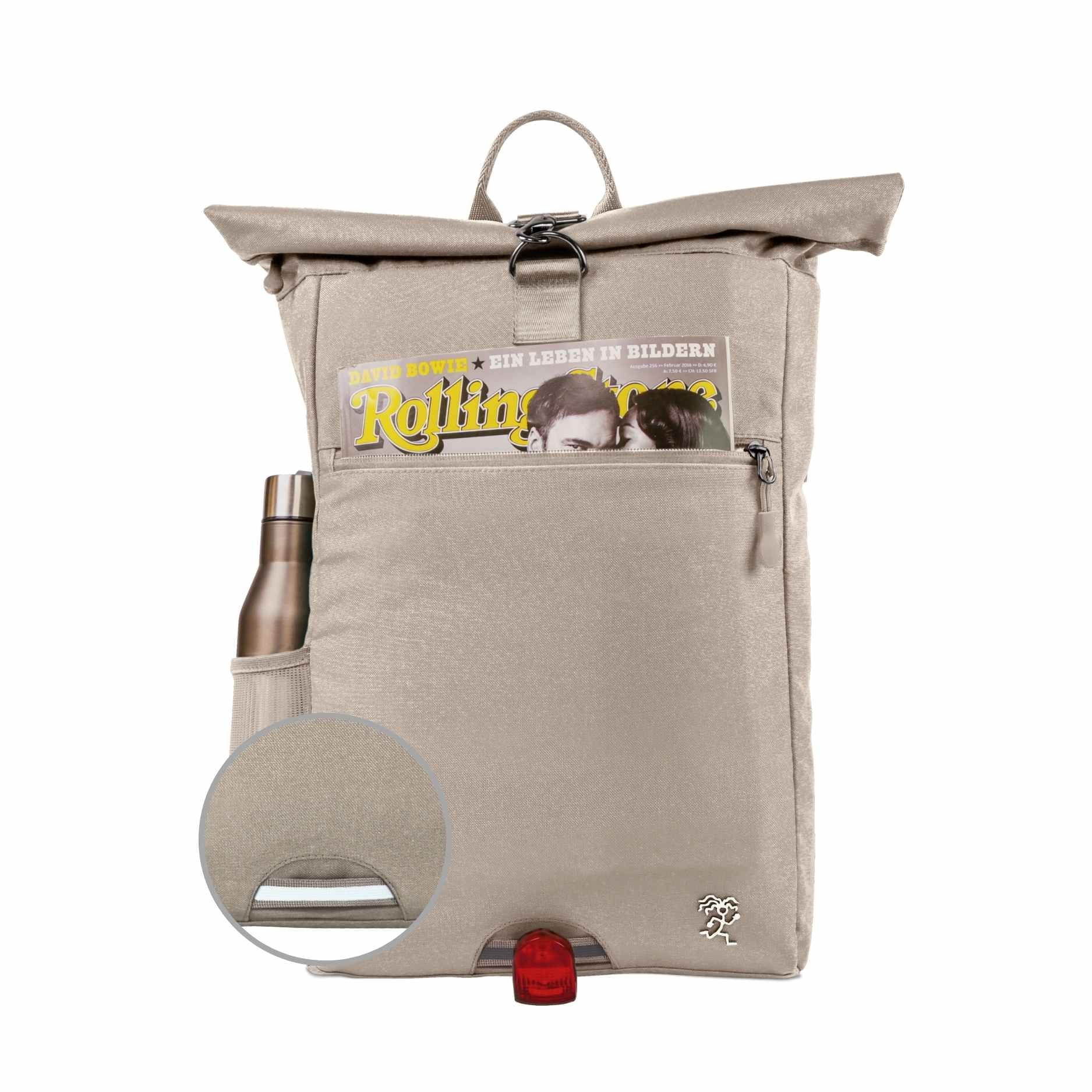 Vorderansicht des bepackten FUCHS und REBELL PIET Rolltop Rucksacks in beige mit Thermoflasche, Magazin und reflektierendem Riemen auf der Vorderseite.