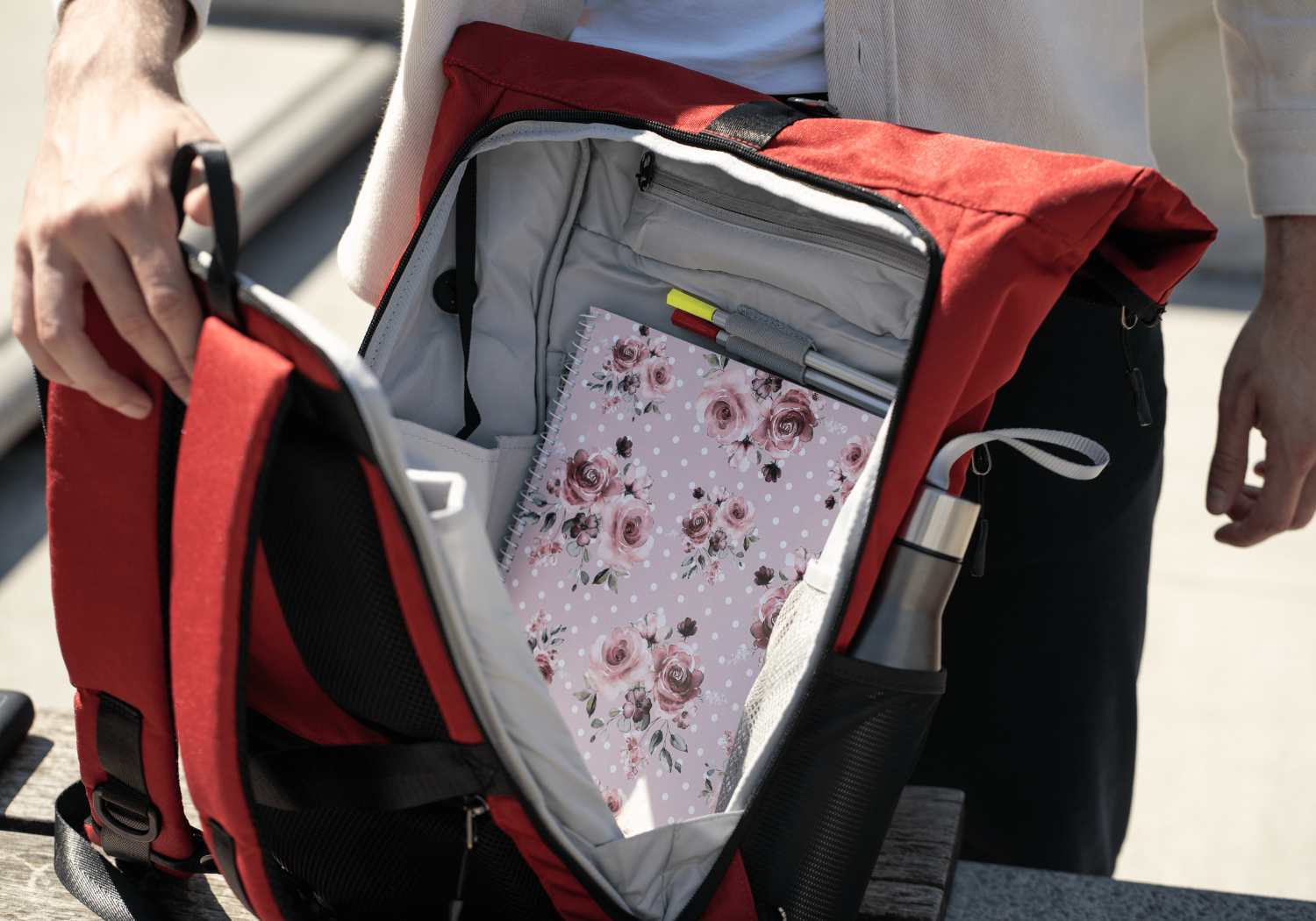 Ein Mann oeffnet den roten FUCHS und REBELL Rucksack PIET ueber den hinteren 2-Wege-Reissverschluss. Durch den hinteren Reissverschluss laesst sich der Rucksack komplett oeffnen. 