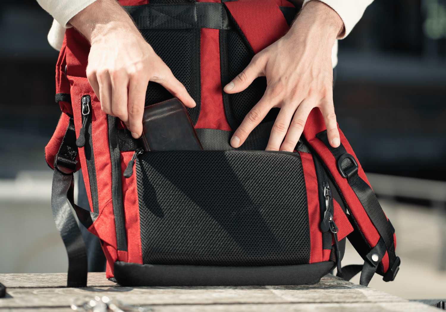 Ein Mann steckt seine Brieftasche in den hinteren Anti-Diebstahl Fach von dem roten FUCHS und REBELL Rolltop Rucksack PIET.