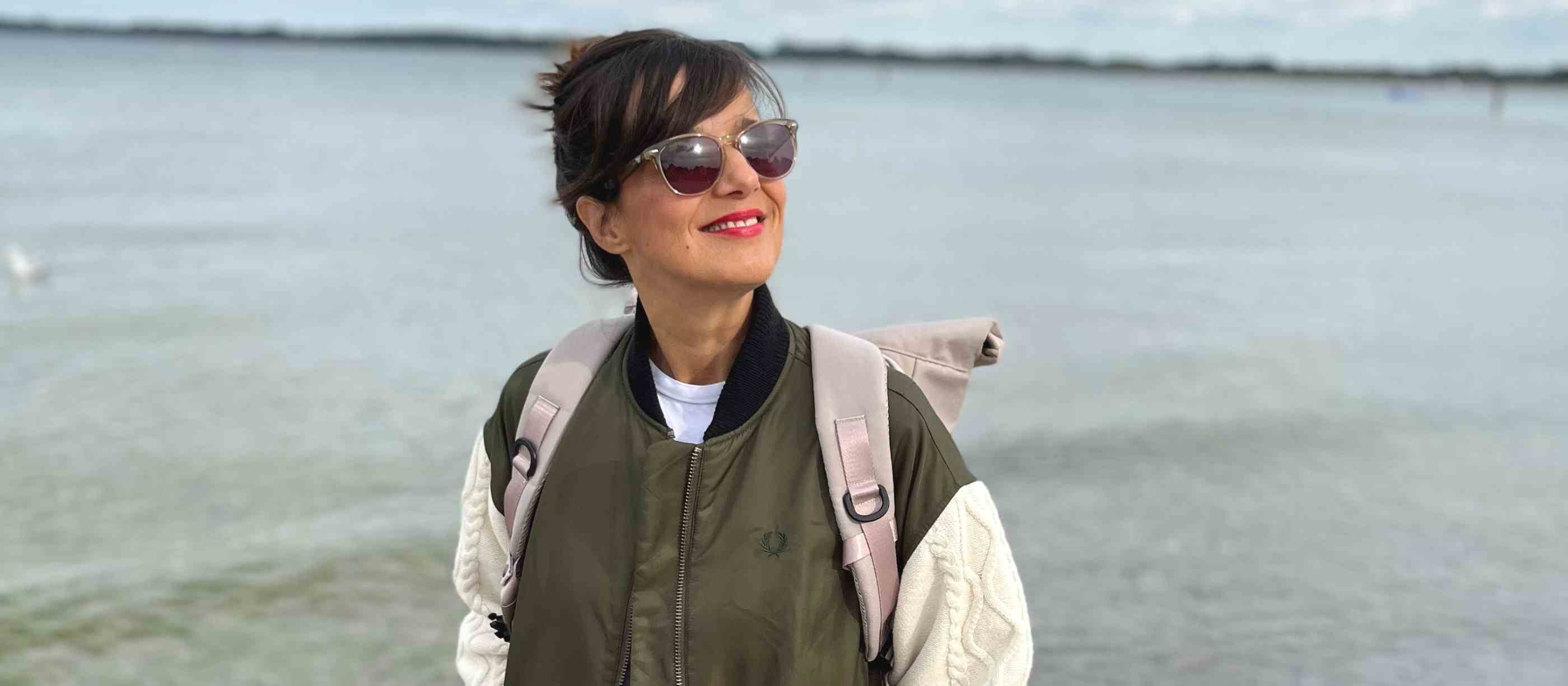 Junge Frau geht am Strand in Travemünde spazieren. Sie traegt den beige farbenen FUCHS und REBELL PIET Rolltop Rucksack.