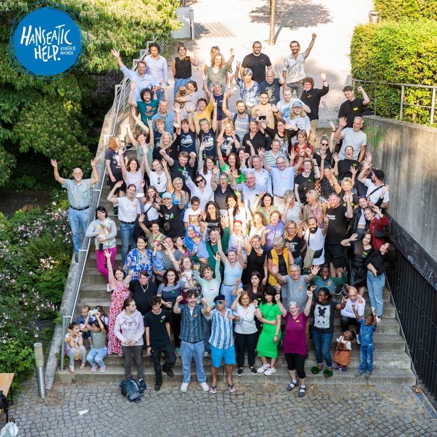 Das Team von Hanseatic Help steht fuer ein Gruppenfoto auf einer Treppe an der Elbe.