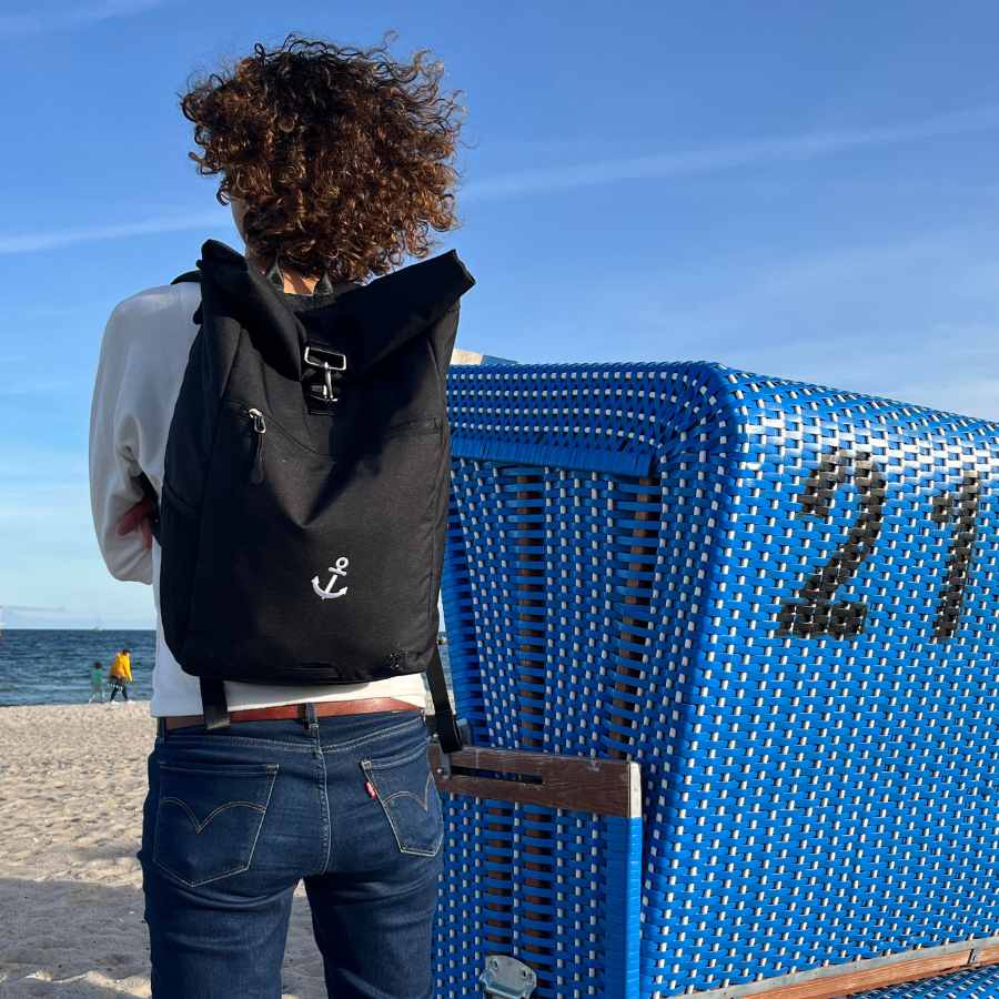 B2B - Frau traegt den gebrandeten FUCHS und REBELL PIET Rolltop Rucksaam Strand. 