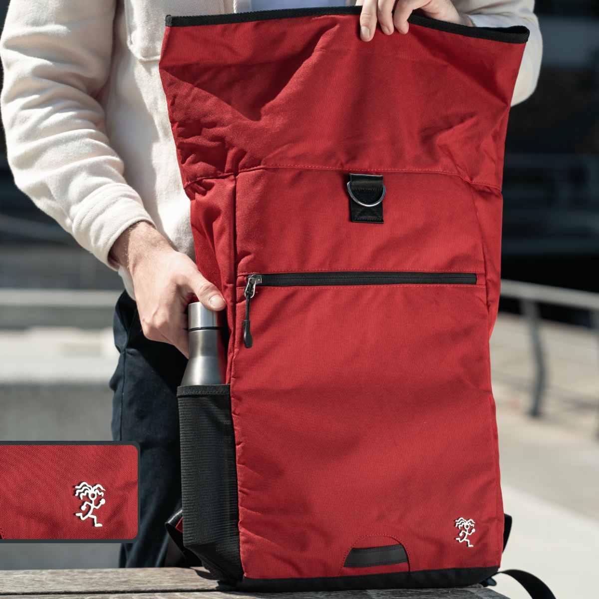 Ein Mann steckt eine Flasche in die Seitentasche des roten FUCHS UND REBELL PIET ROLLTOP RUCKSACKS