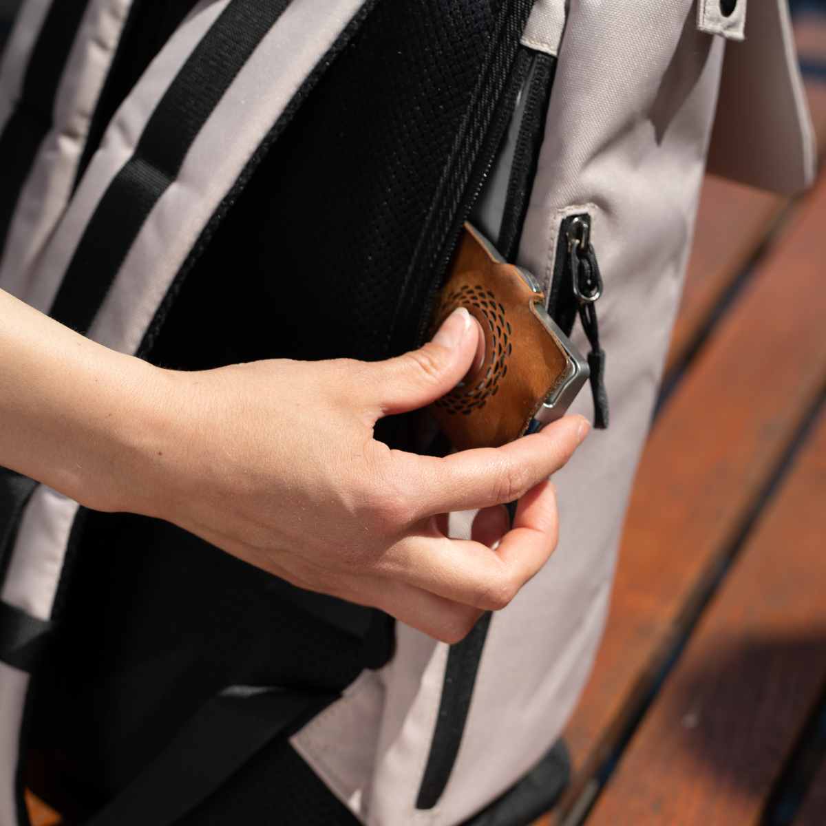 Eine Frau nimmt ihr Portemonnaie aus dem Anti-Diebstahl Fach des beigefarbenen FUCHS und REBELL MATS Daypack Rucksacks