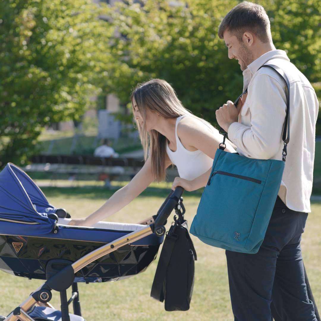 Junges Paar geht im Park spazieren mit ihrem Baby. Beide tragen die FUCHS und REBELL JONA Umhängetaschen.