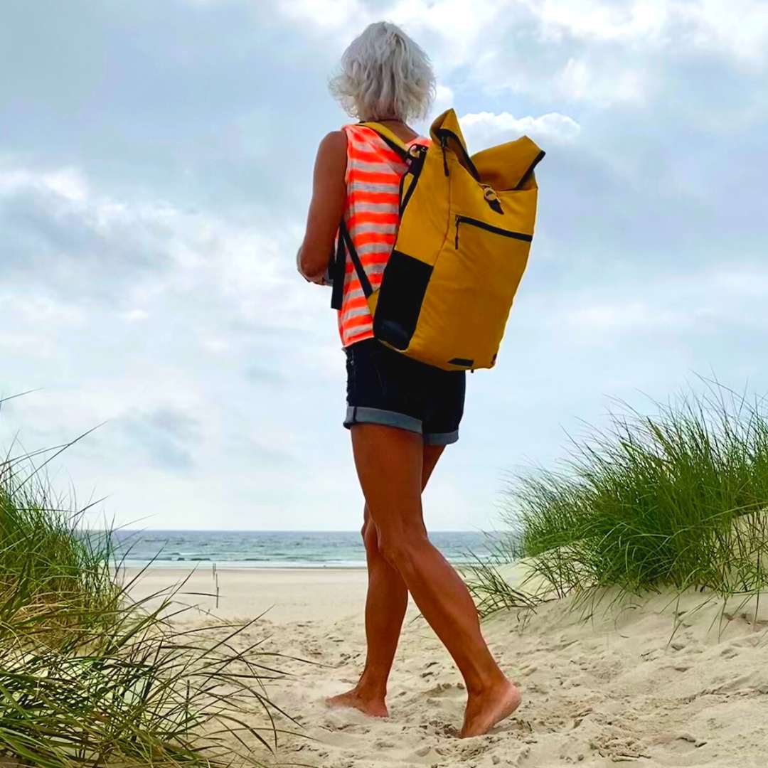 FRau geht am Strand spazieren und traegt den gelben FUCHS UND REBELL PIET Rucksack