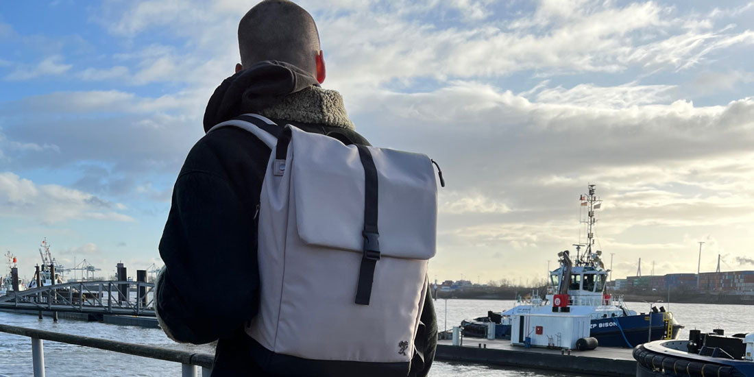 Mann geht an der Elbe spazieren und traegt den beigefarbenen MATS Rucksack von FUCHS und REBELL