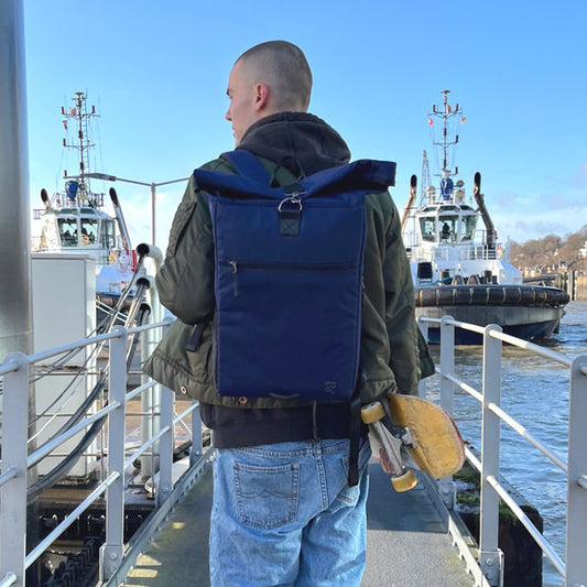 Gutaussehender Mann geht mit dem dunkelblauen PIET Rolltop Rucksack an der Elbe spazieren.