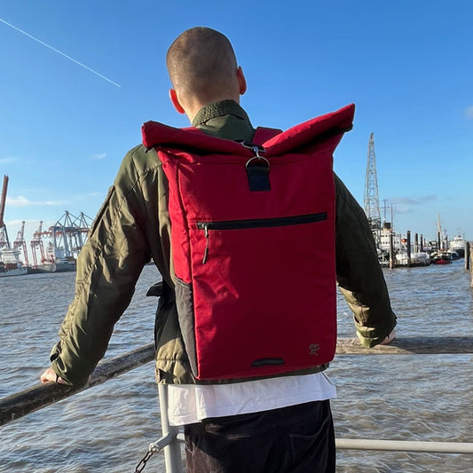 Gutaussehender Mann geht mit dem roten PIET Rolltop Rucksack an der Elbe spazieren.