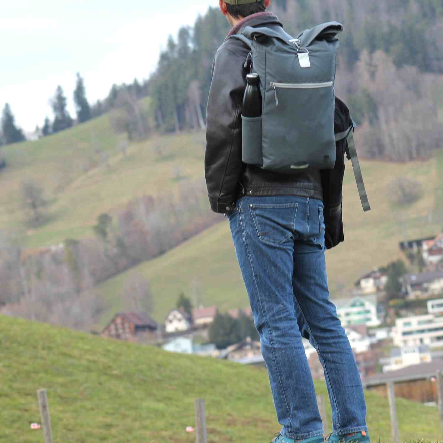 Mann traegt den FUCHS und REBELL PIET Rolltop Rucksack in dunkelgrau. 
