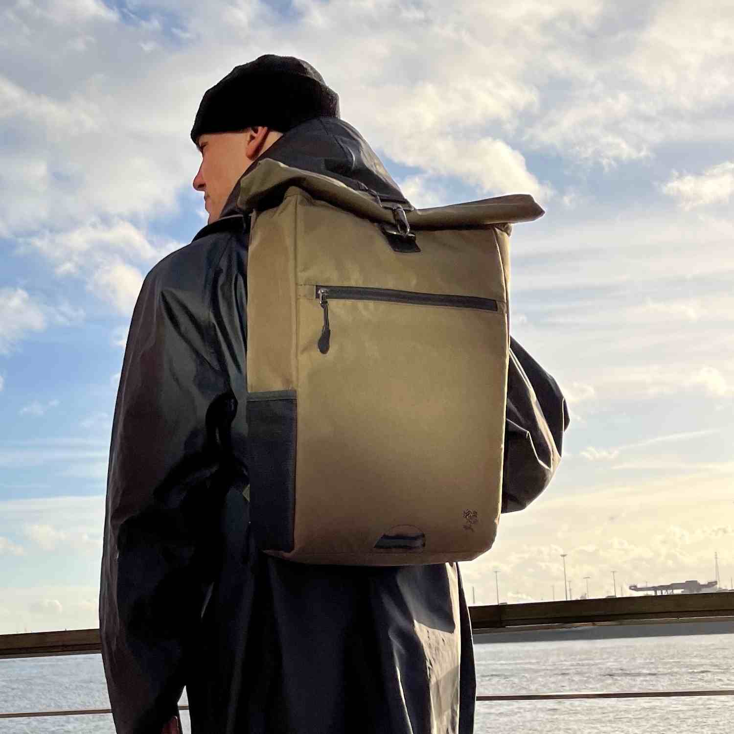 Mann traegt den FUCHS und REBELL PIET Rolltop Rucksack in gruen. 