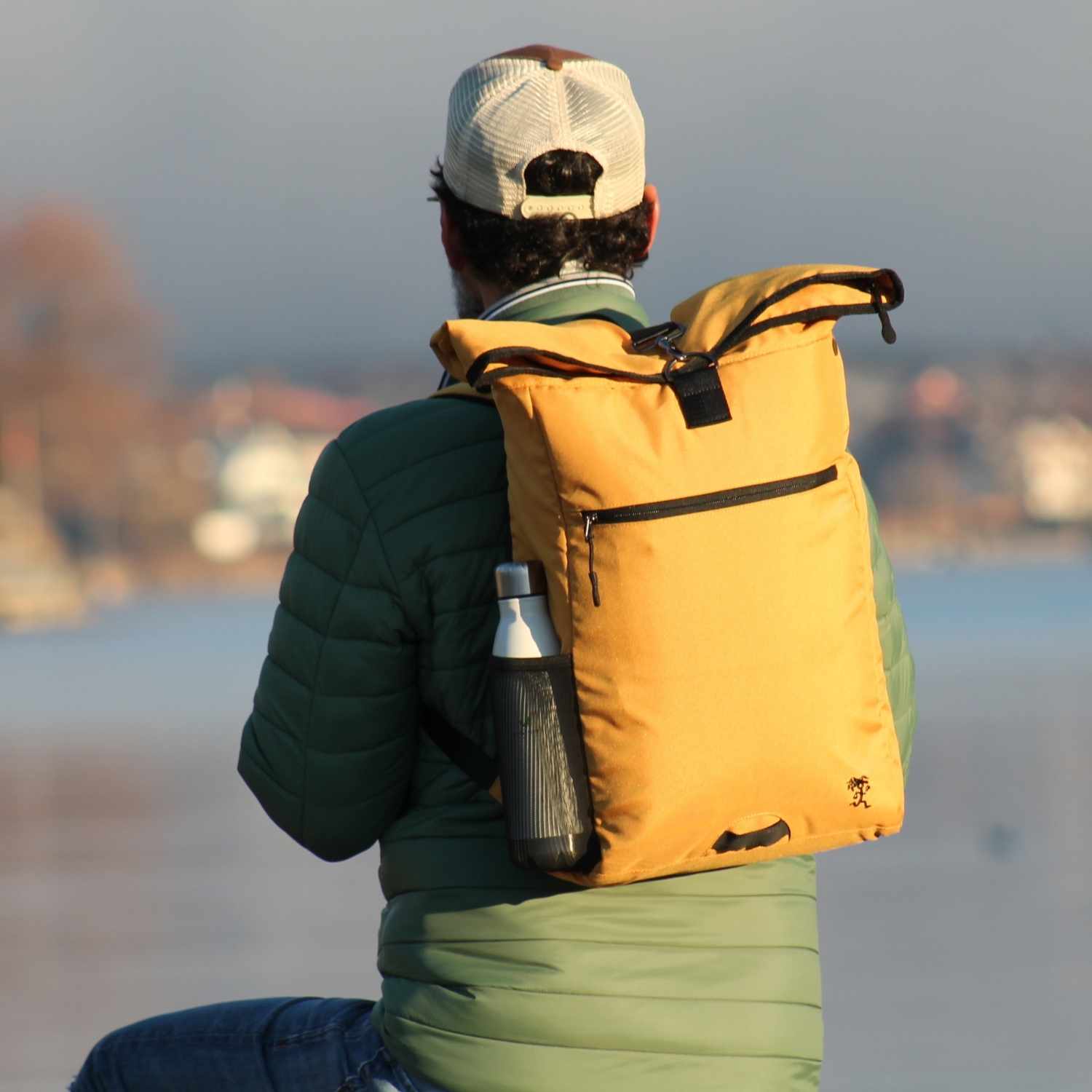 Mann traegt den FUCHS und REBELL PIET Rolltop Rucksack in gelb.