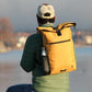 Gutaussehender Mann sitzt am Züricher See mit dem senfgelben PIET Rolltop Rucksack.