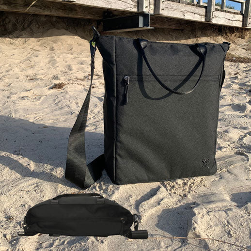 Vorderansicht der schwarzen FUCHS und REBELL JONA Umhaengetasche am Strand mit Blick auf den Hauptreißverschluss, um die Diebstahl-Sicherheit der Tasche zu zeigen.