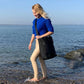 Junge Frau geht am Strand spazieren und traegt die schwarze FUCHS und REBELL JONA Umhaengetasche.
