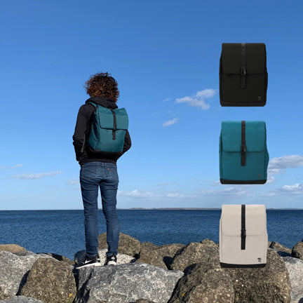 Junge Frau spaziert am Strand mit dem petrolfarbenen MATS Daypack Rucksack und zeigt die drei verschiedenen Rucksack Farben.
